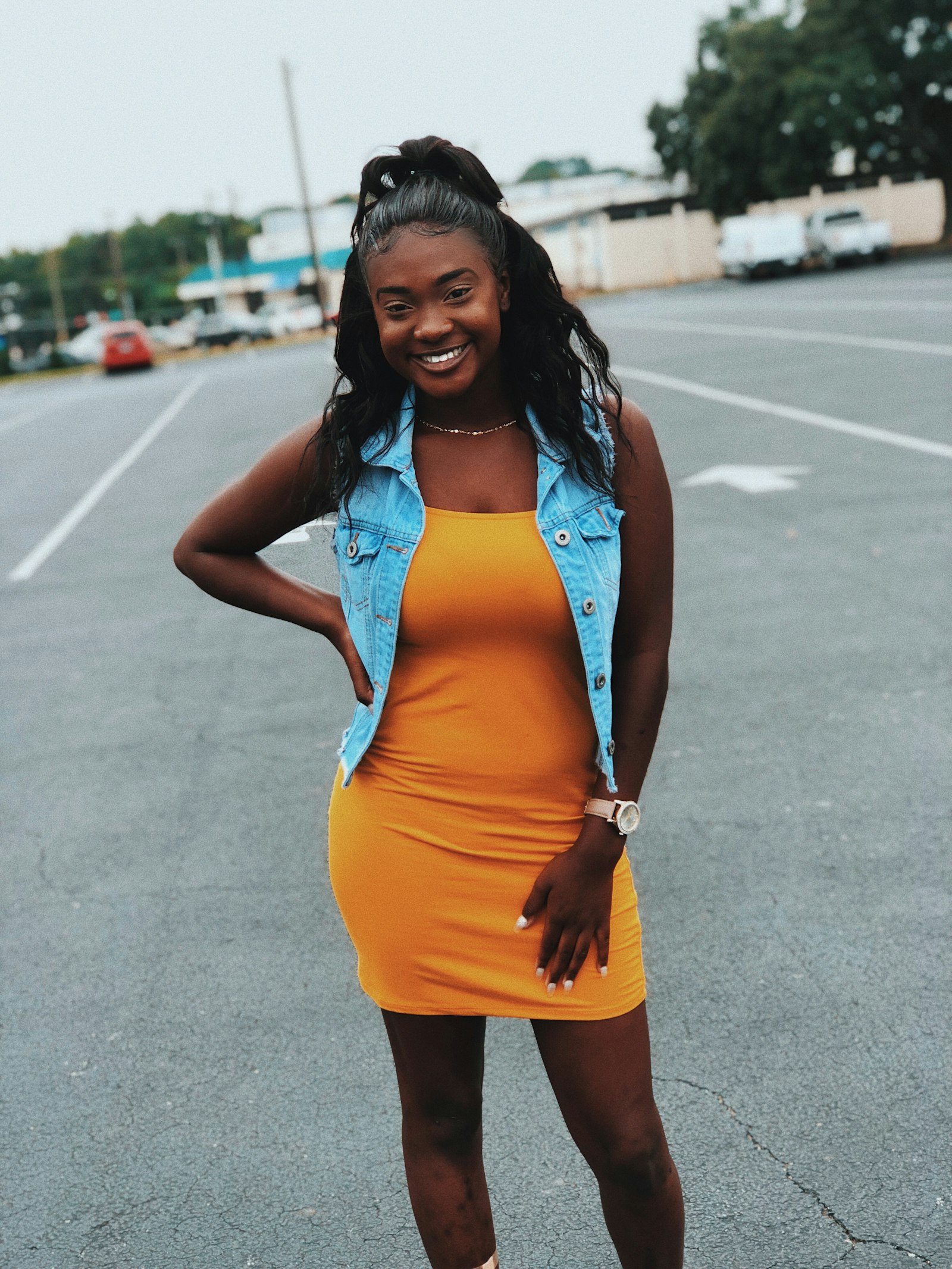A woman in an orange dress layered with a blue denim vest